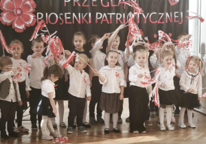 Dzieci śpiewają piosenkę patriotyczną i machają wstęgami biało - czerwonymi