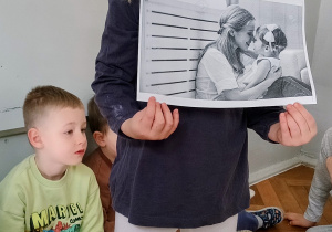 Dziewczynka stoi i pokazuje ilustracje innym dzieciom.