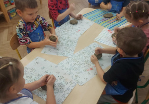 dzieci siedzą przy stoliku i w dłoniach uplastyczniają glinę