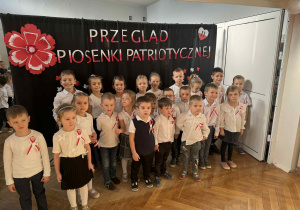 Zdjęcie przedstawia dzieci stojące na tle napisu "Przegląd patriotyczny.