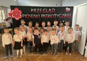 Zdjęcie przedstawia dzieci stojące na tle napisu "Przegląd patriotyczny.