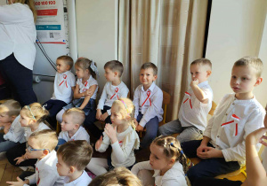 Zdjęcie przedstawia dzieci siedzące na krzesłach przed występem.