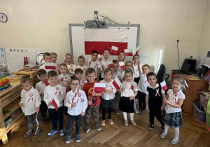 Zdjęcie przedstawia dzieci z flagami w rękach, na tle polskiej flagi.