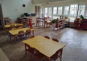 na zdjęciu widać salę przedszkolną grupy trzeciej, na podłodze znajduje się wyklejona elipsa, niskie regały z materiałem rozwojowym dla dzieci, żółte stoliki do pracy