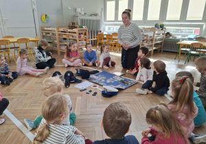 kobieta stoi przed grupą dzieci, na podłodze leżą atrybuty policjanta