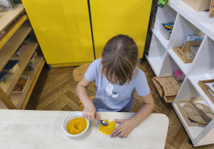 Na zdjęciu widzimy dziewczynkę, która smaruje kawałek wafla dżemem dyniowym.