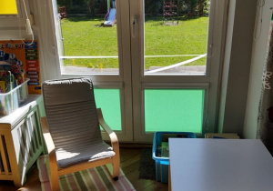 na zdjęciu widać fotel dla dzieci, biały stolik oraz okno balkonowe