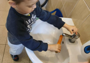 Na zdjęciu widzimy chłopca, który myje marchewkę.