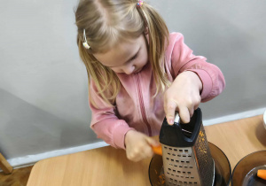 Na zdjęciu widzimy dziewczynkę, która trze marchewkę na grubych oczkach.