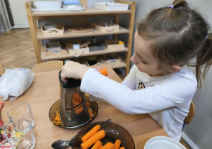 Na zdjęciu widzimy dziewczynkę, która trze marchewkę na grubych oczkach.