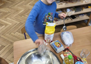 Na zdjęciu widzimy chłopca, który odmierzoną ilość mąki wsypuje do miski.