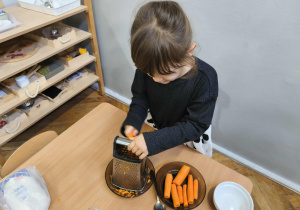 Na zdjęciu widzimy dziewczynkę, która trze marchewkę.