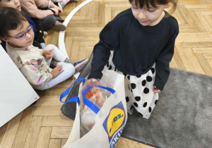 Na zdjęciu widzimy dziewczynkę, która wyjmuje z torby składnik potrzebny do ciasta marchewkowego.