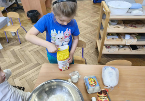 Na zdjęciu widzimy chłopca, który odmierza za pomocą szklanki odpowiednią ilość mąki.