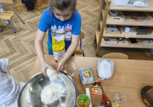 Na zdjęciu widzimy chłopca, który odmierzoną ilość mąki wsypuje do miski.