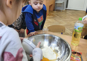 Na zdjęciu widzimy dziewczynkę, która wlewa rozbite jajko do dużej miski. Poprzednio jajko zostało rozbite w mniejszej misce.