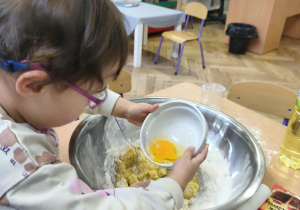 Na zdjęciu widzimy dziewczynkę, która wlewa rozbite jajko do dużej miski. Poprzednio jajko zostało rozbite w mniejszej misce.