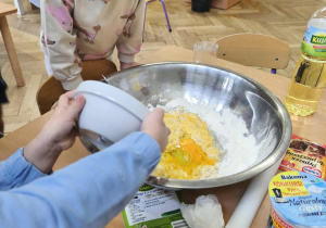 Na zdjęciu widzimy chłopca, który wlewa rozbite jajko do dużej miski. Poprzednio jajko zostało rozbite w mniejszej misce.