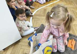 Na zdjęciu widzimy dziewczynkę, która wyjmuje z torby składnik potrzebny do ciasta marchewkowego.