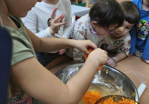 Na zdjęciu widzimy dziewczynkę, która wkłada do dużej miski marchewkę wcześniej ztarkowaną.