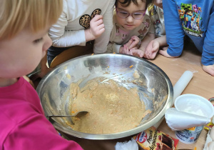 Na zdjęciu widzimy dziewczynkę, która wkłada do dużej miski marchewkę wcześniej ztarkowaną.
