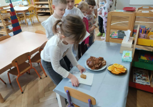 Na zdjęciu widzimy dziewczynkę, która wybiera kawałek ciasta marchewkowego, aby go zjeść.