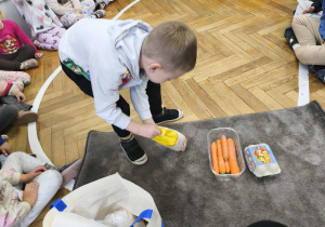 Na zdjęciu widzimy chłopca, który wyjął jeden ze składników ciasta marchewkowego z torby.