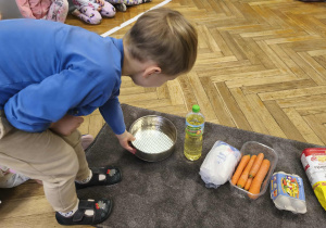 Na zdjęciu widzimy chłopca, który na dywanik z produktami do upieczenia ciasta wykłada foremkę.
