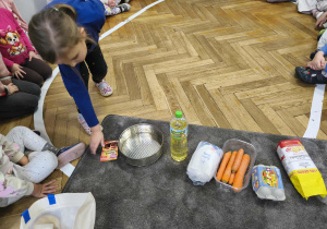 Na zdjęciu widzimy dziewczynkę, która wyjęła jeden ze składników ciasta marchewkowego z torby.