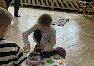 Zdjęcie przedstawia dziewczynkę wlewającą psu wodę do miski.