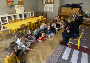 Zdjęcie przedstawia dzieci siedzące w grupie i rozmawiające z Paniami.