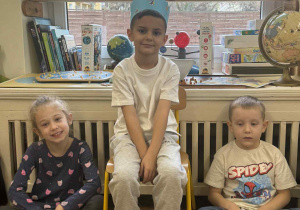 Zdjęcie przedstawia chłopca w koronie, siedzącego na krześle, między dziećmi.