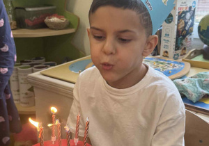 Zdjęcie przedstawia chłopca dmuchającego świeczki.