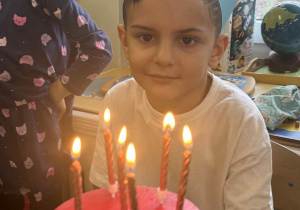 Zdjęcie przedstawia chłopca przy torcie urodzinowym z zapalonymi świeczkami.