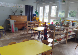 na zdjęciu widać salę przedszkolną grupy pierwszej, stoliki z żółtymi blatami, niskie regały z materiałem rozwojowym dla dzieci