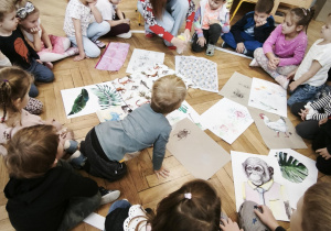 Dzieci siedzą w kręgu i oglądają tkaniny przyniesione przez gościa