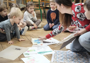 Dzieci siedzą w kręgu i oglądają tkaniny przyniesione przez gościa