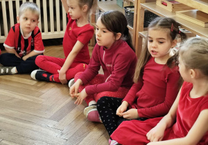 Dzieci ubrane na czerwono siedzą w kręgu.