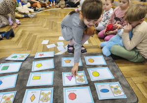 Na zdjęciu widzimy dziecko, które dopasowuje ilustrację misia do jego kształtu na brzuchu.