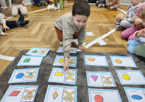 Na zdjęciu widzimy dziecko, które dopasowuje ilustrację misia do jego kształtu na brzuchu.