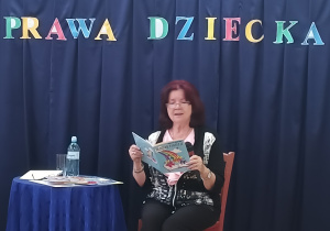 Poetka siedzi na krześle i czyta swoje wiersze.