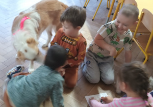 Dzieci siedzą obok psa na podłodze.