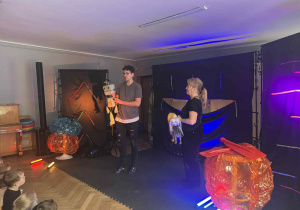 Zdjęcie przedstawia aktorów na scenie trzymających w rękach kukiełki.