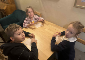 Zdjęcie przedstawia dzieci siedzące przy stolikach. Dzieci jedzą ciastka.