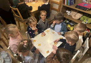 Zdjęcie przedstawia dzieci siedzące przy stolikach. Na stolikach leżą ciasteczka.