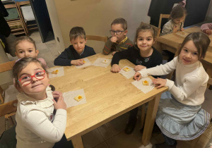 Zdjęcie przedstawia dzieci siedzące przy stolikach. Na stolikach leżą ciasteczka.
