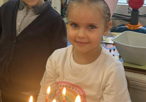 Zdjęcie przedstawia dziewczynkę przy torcie z zapalonymi świeczkami.