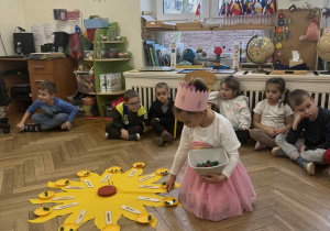Zdjęcie przedstawia dziewczynkę rozkładającą koraliki na słoneczku urodzinowym.