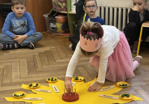 Zdjęcie przedstawia dziewczynkę wkładającą świeczkę w drewniany tort.