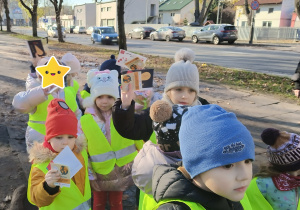 Dzieci stoją na ulicy i trzymają w rękach ulotki.